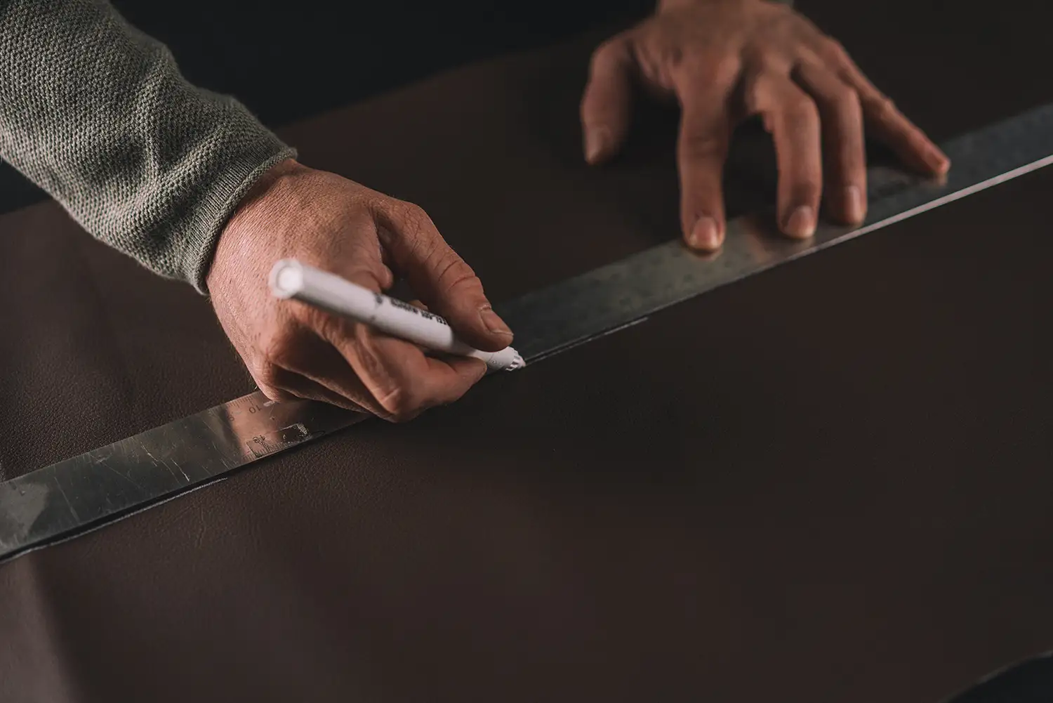 Hände beim Anzeichnen einer Schnittlinie auf Leder