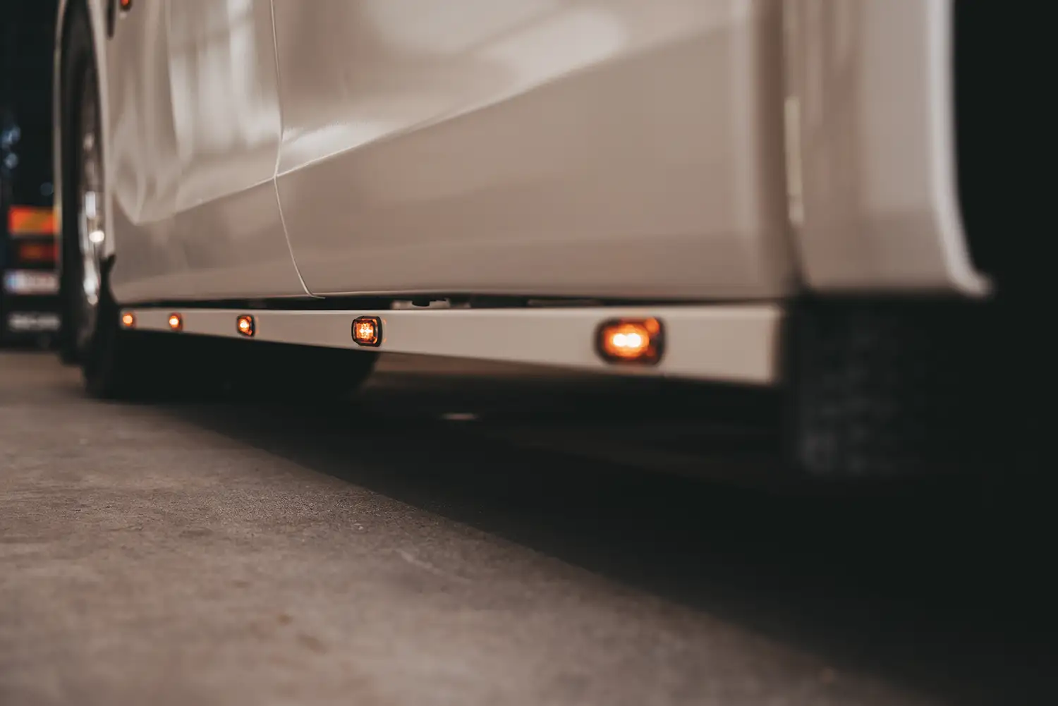 Seitenansicht eines weißen LKWs mit leuchtenden orange-gelben Seitenmarkierungsleuchten auf dunklem Asphalt bei Nacht